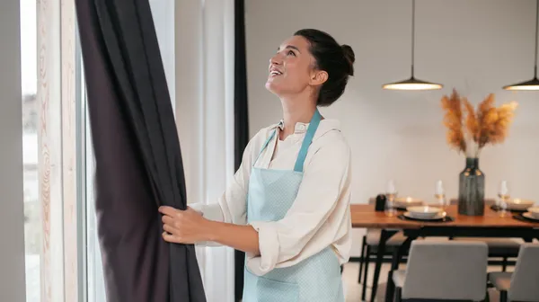 1767967612-young-woman-standing-near-widnow-fixing-curtains