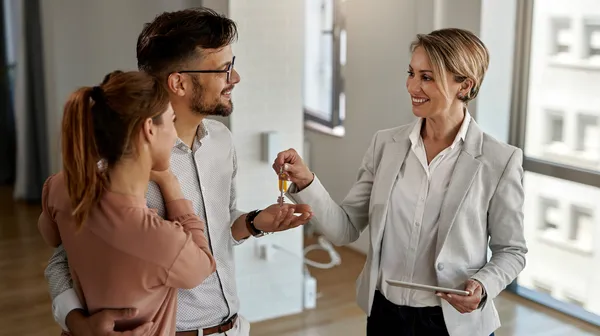 1759474048-happy-real-estate-agent-giving-keys-couple-who-is-buying-their-new-home