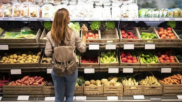 Good looking woman standing front vegetable shelves choosing what buy