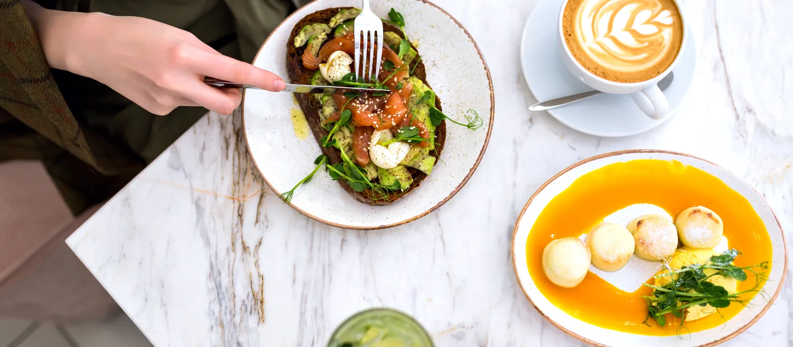 Woman eating her tasty brunch hipster cafe top view marble table salmon avocado toast coffee sweet tasty cheesecakes enjoying her breakfast