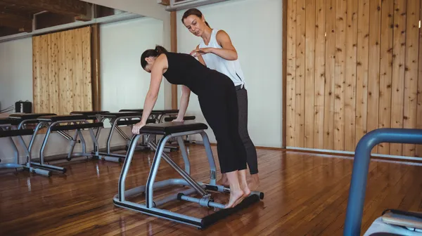 Trainer helping woman while practicing pilates