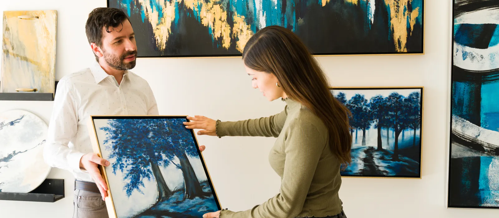 Male artist showing his painting female client interested buying some artwork from exihibiton art gallery