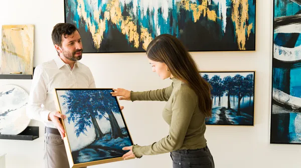 Male artist showing his painting female client interested buying some artwork from exihibiton art gallery