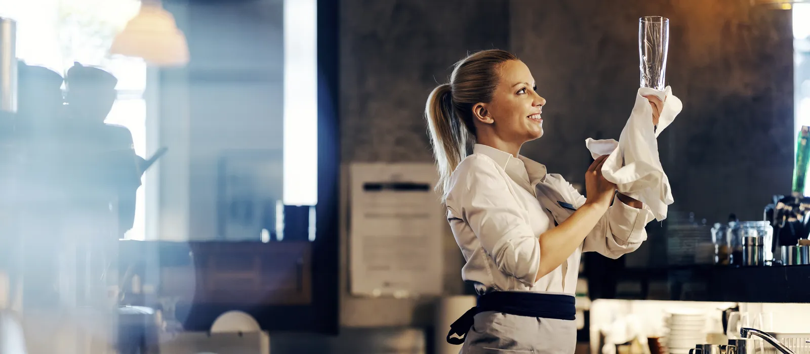 Happy bartender is wiping beer glass while standing bar