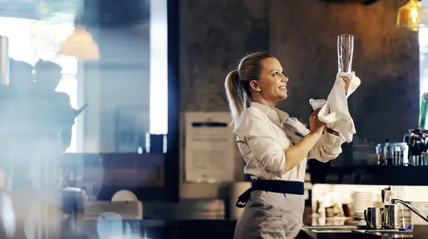 Happy bartender is wiping beer glass while standing bar