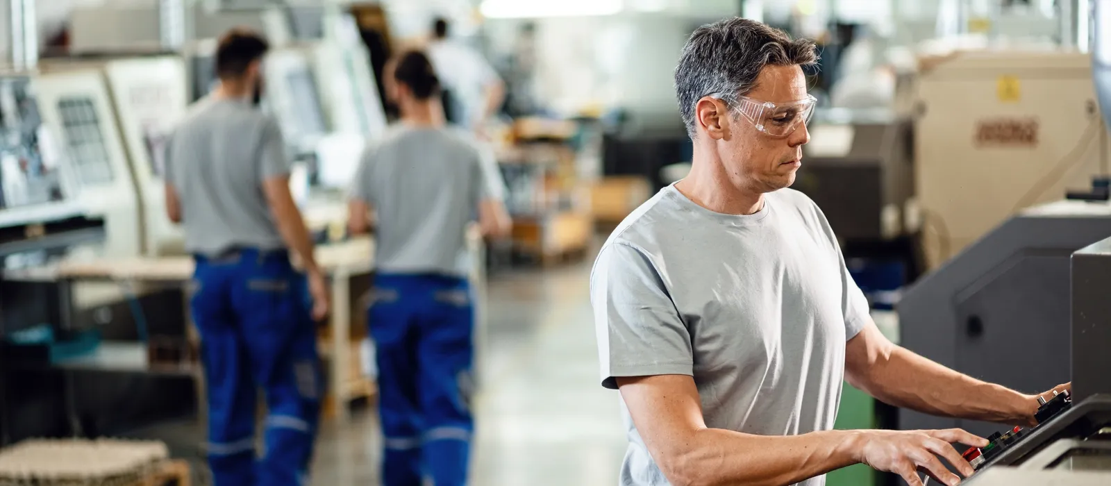 Mid adult worker operating cnc machine while working industrial facility