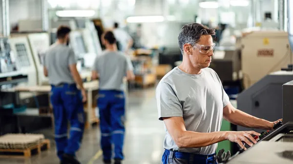Mid adult worker operating cnc machine while working industrial facility