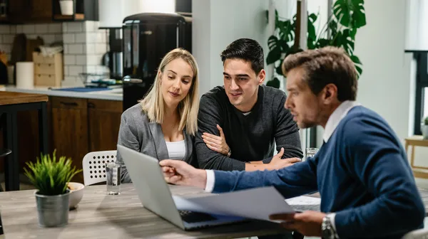 Young couple real estate agent using laptop while going through housing plan meeting
