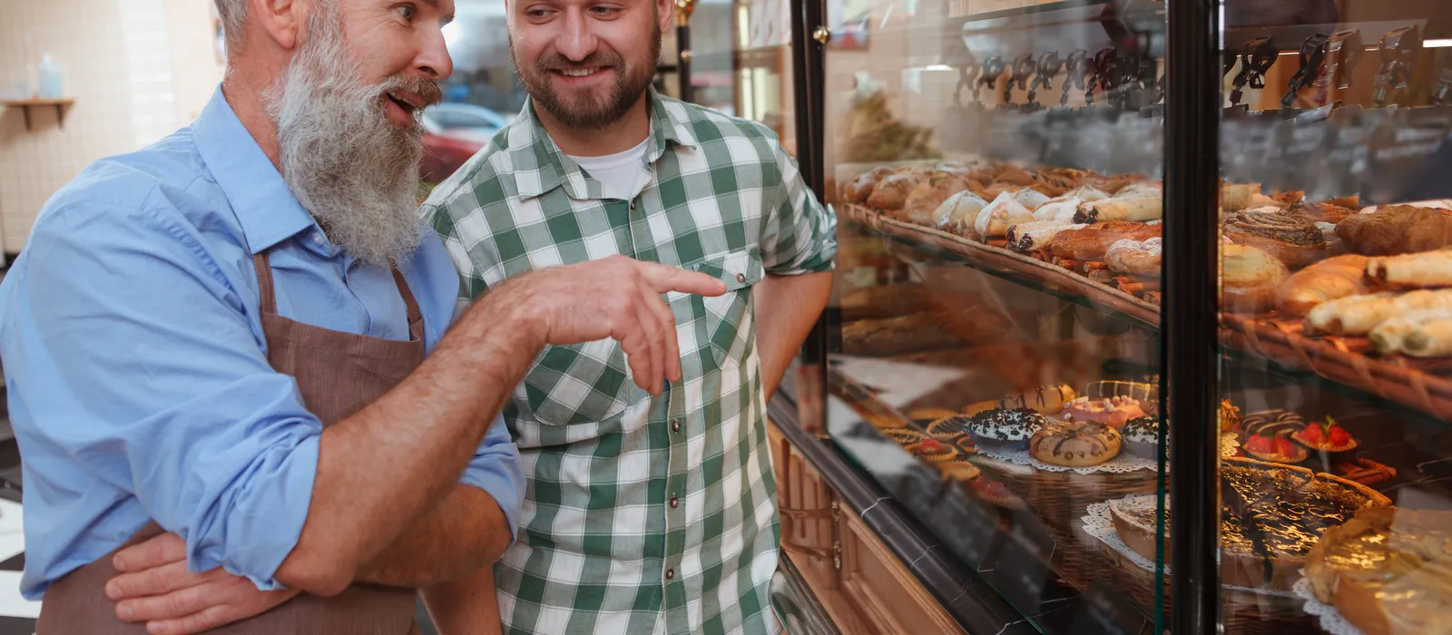 Young man talking senior baker while shopping pastry local bakery